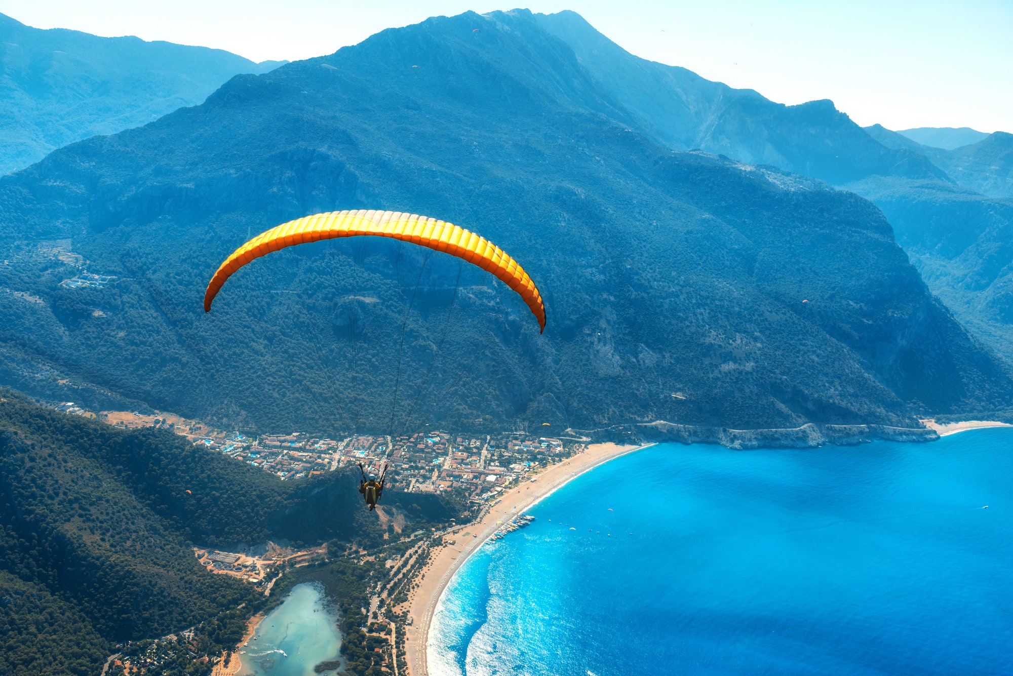 Paraglider tandem flying over the sea with blue water and mountains